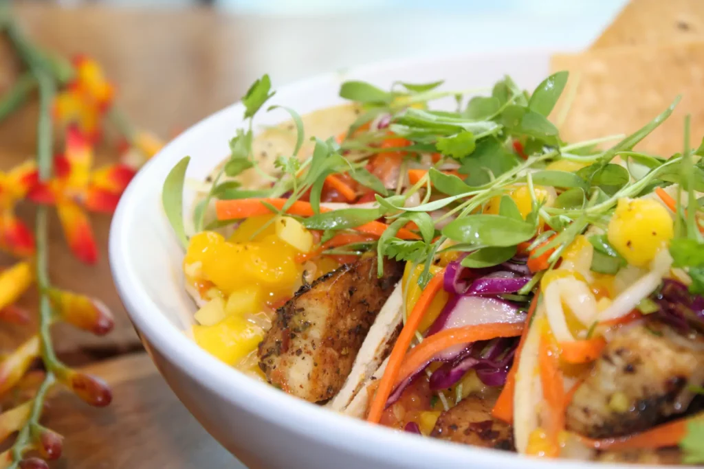 A colorful salad in a white bowl with grilled chicken, mango, cabbage, carrots, and fresh greens.