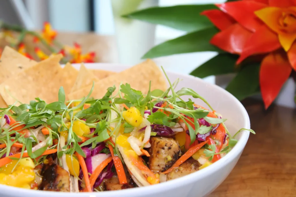 Bowl of colorful vegetable salad with grilled chicken and tortilla chips, garnished with greens.
