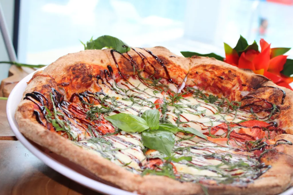 Close-up of a pizza topped with fresh basil, tomato slices, cheese, and a drizzle of balsamic glaze.