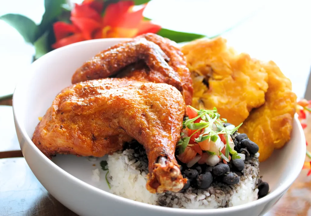 Grilled chicken with rice, black beans, pico de gallo, and plantains in a white bowl.